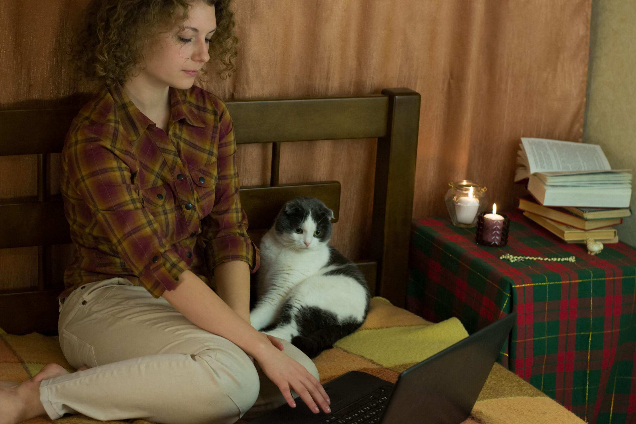 A curly-haired woman is sitting on a bed, reading about emotional support animal laws in Delaware on her laptop, with a cat resting by her side.