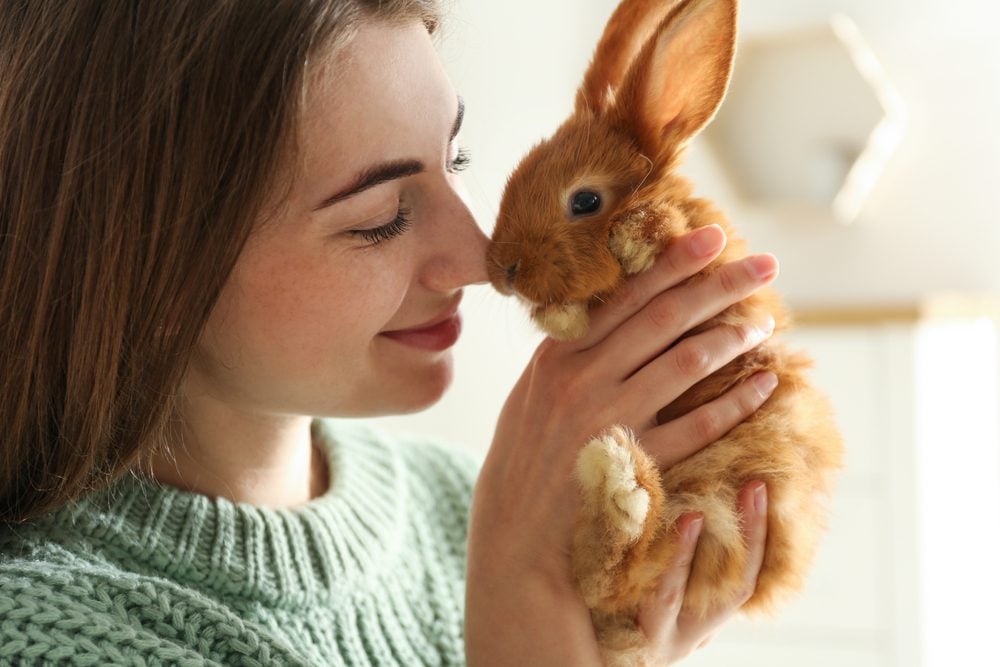 Smiling woman holds brown rabbit up to her face