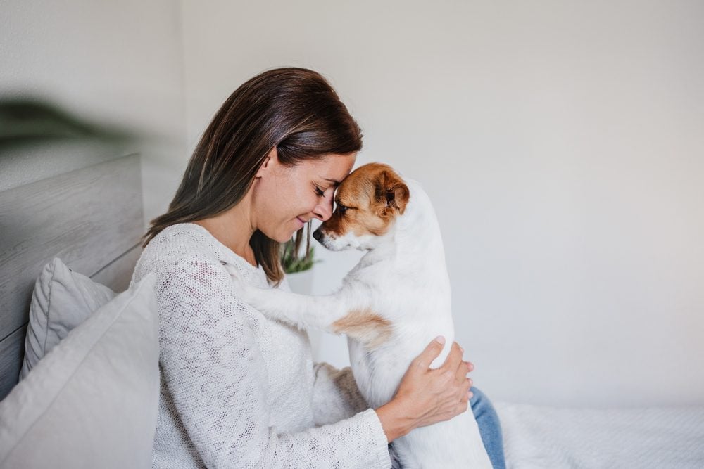 Brunette woman presses her forehead against a dog’s forehead