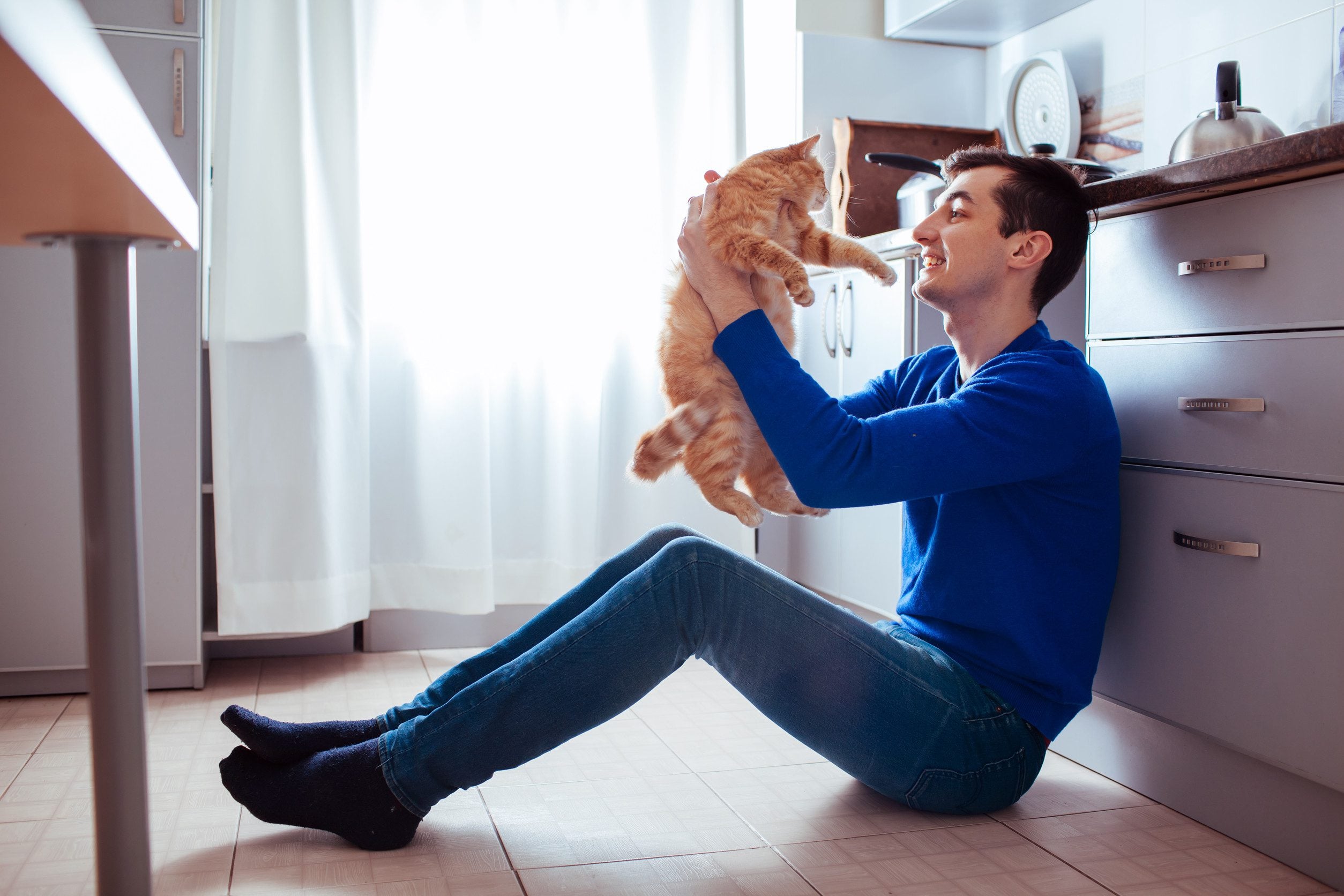 Man sitting on the kitchen floor holding up his cat, illustrating how an ESA letter in Indianapolis supports keeping companion animals at home.