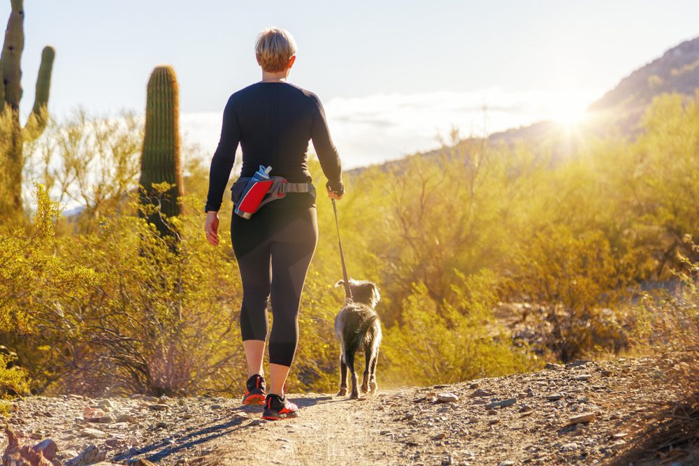 woman walking dog on desert trail