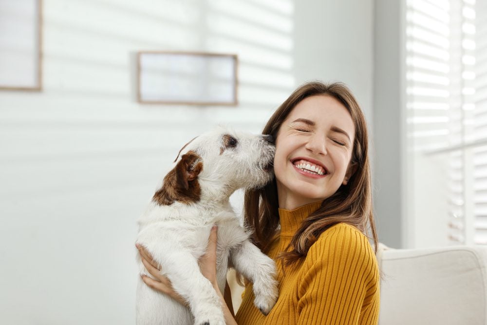 dog licks smiling woman’s cheek