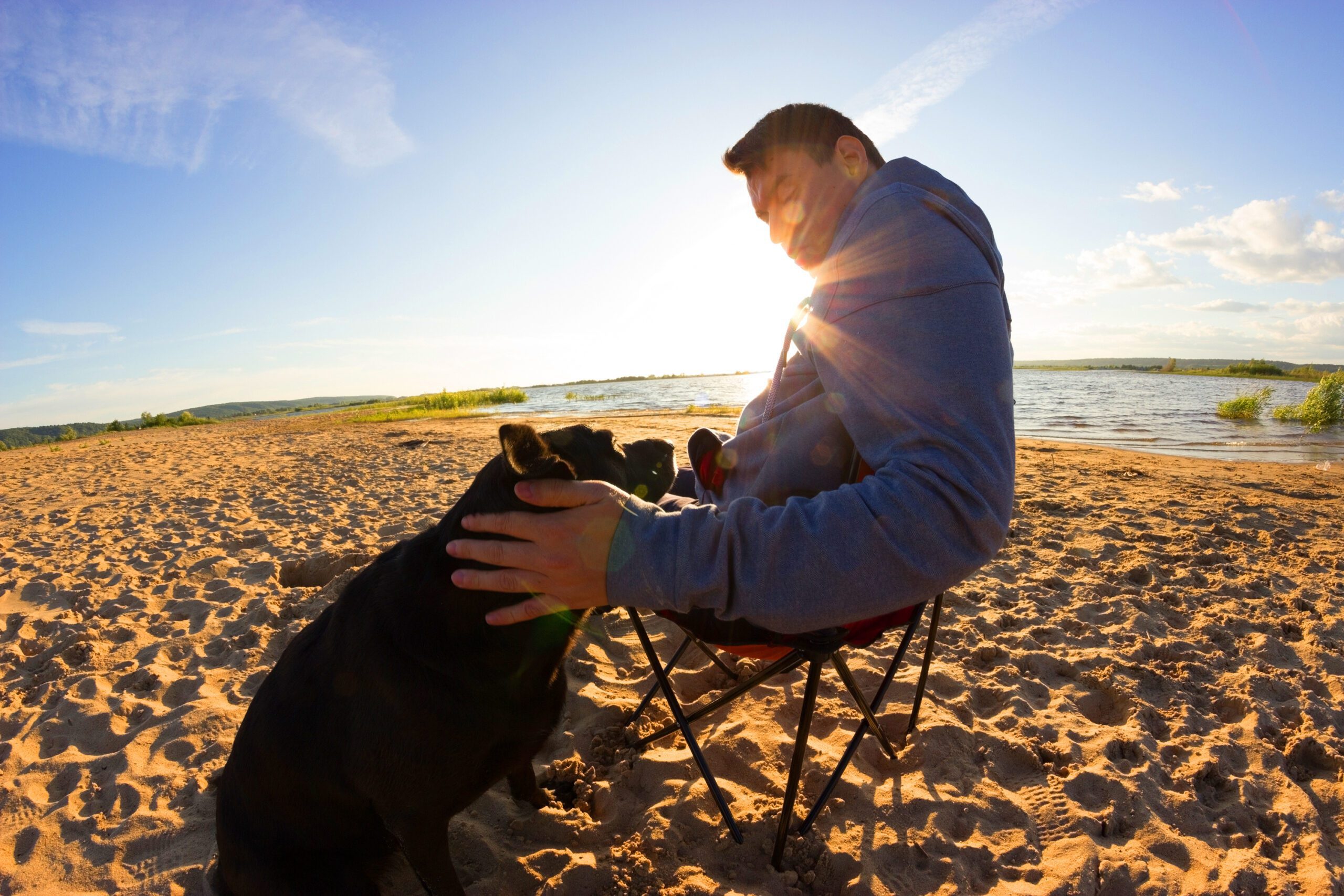 A man in a hoodie sitting at the beach with an emotional support dog in Oakland.