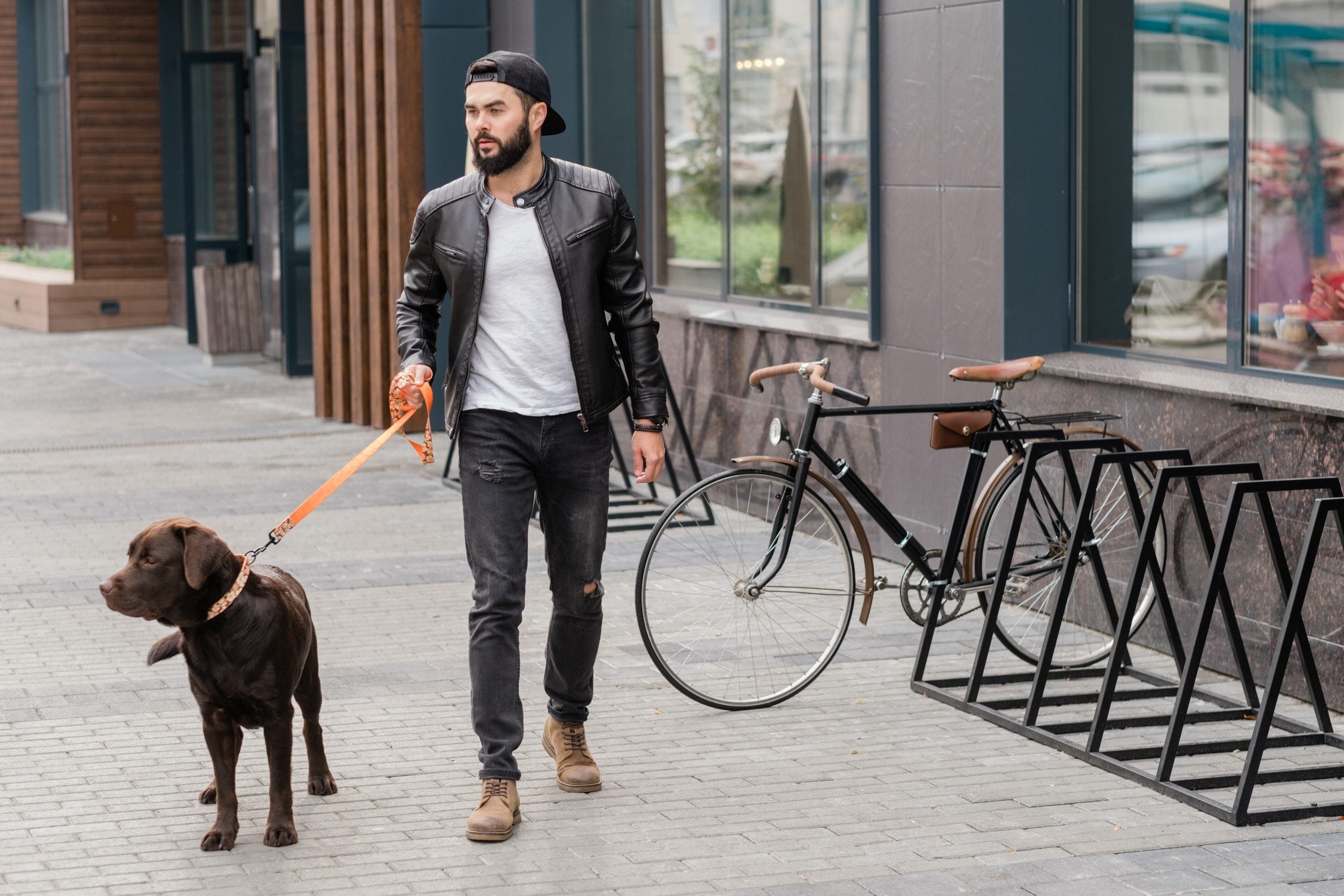 A man holding a black Labrador on a leash, standing in front of a shop in Anaheim.