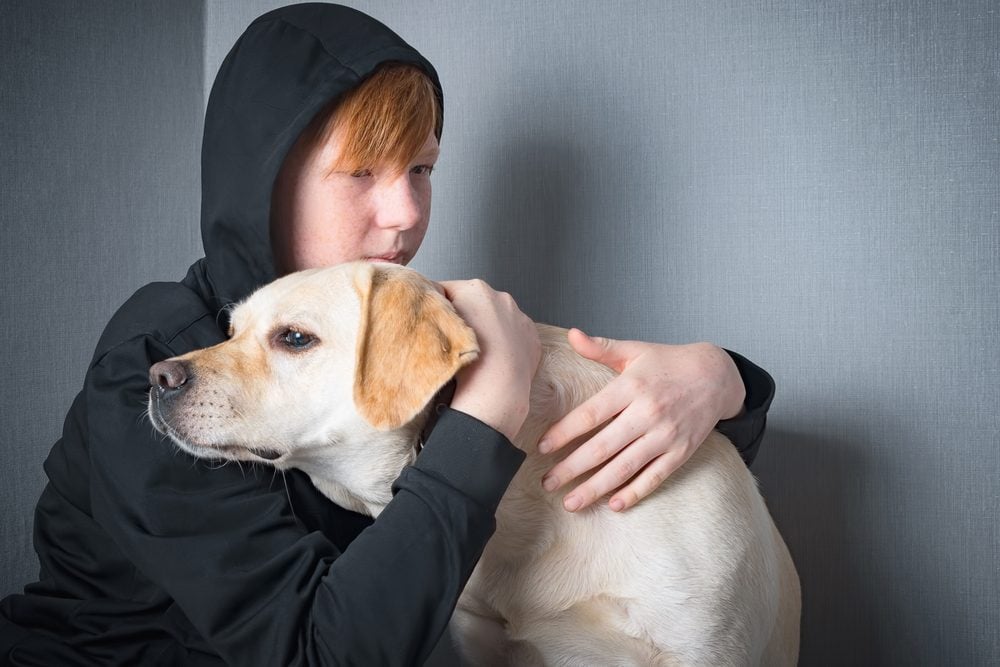 A teenager wearing a black jacket hugging their emotional support animal – a Labrador retriever – in Anchorage, AK.