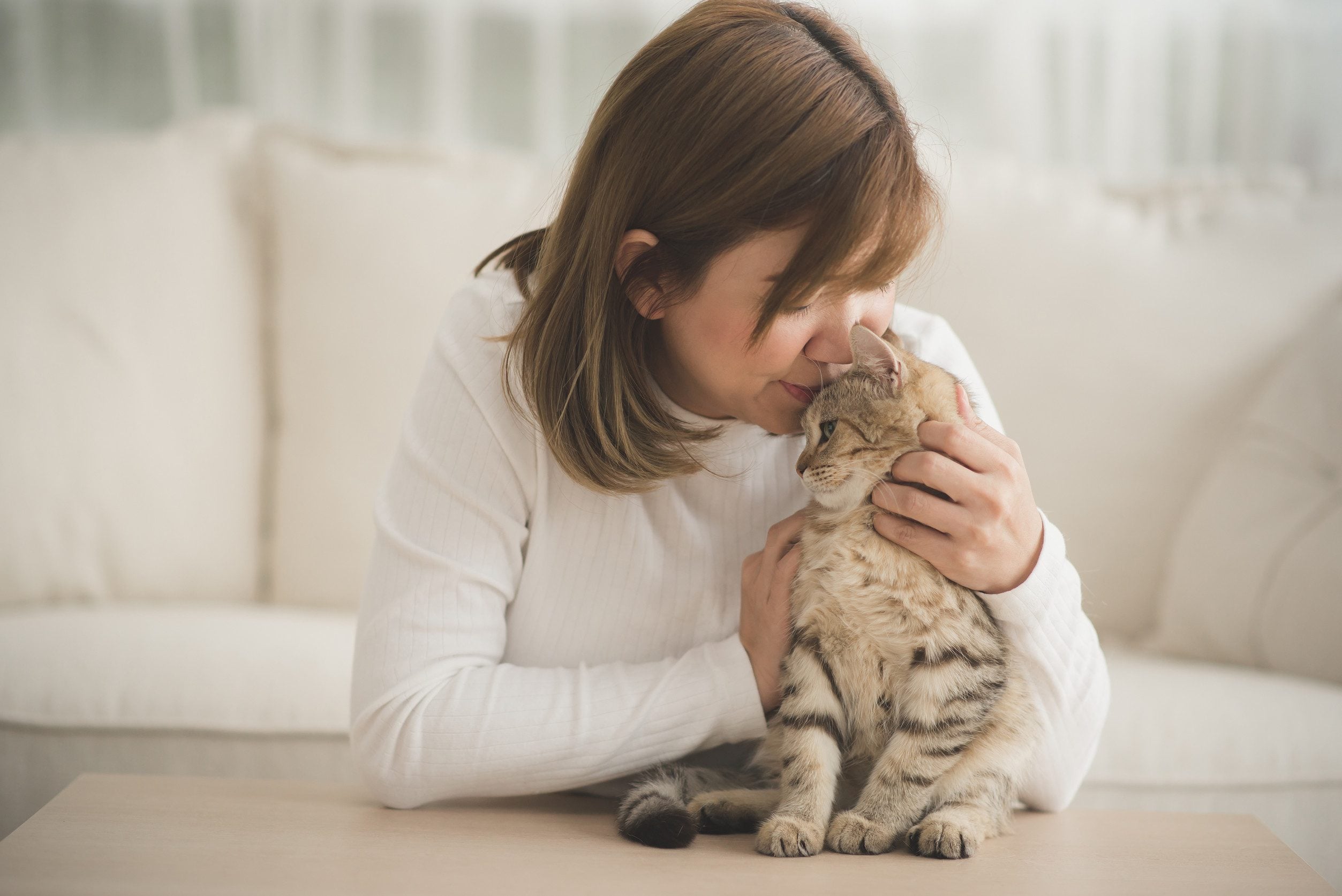 A woman in a white sweater lovingly presses her forehead against her emotional support animal in Stamford, CT.