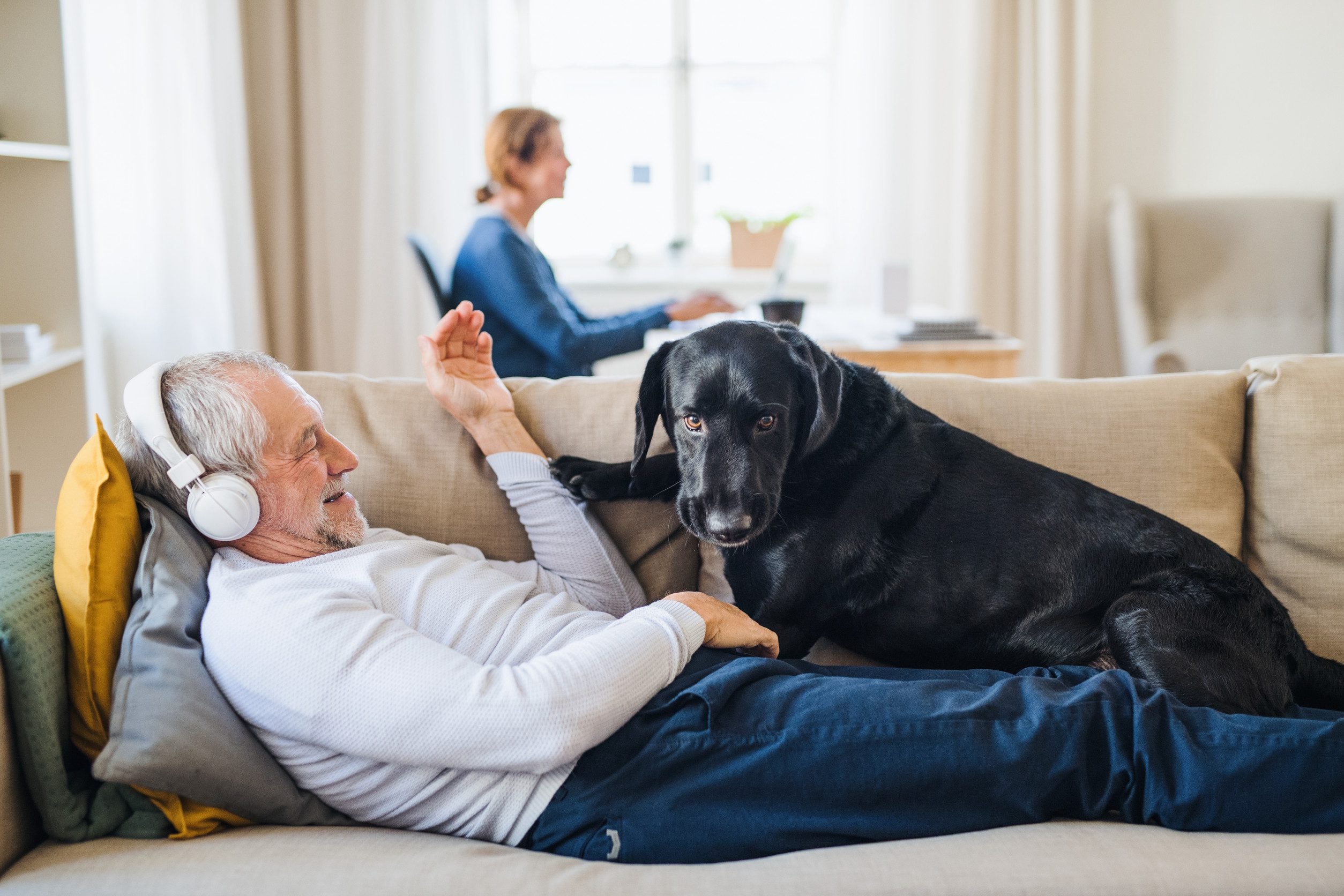 A happy man relaxing with his black emotional support animal dog on a couch in his home in Norfolk, VA.