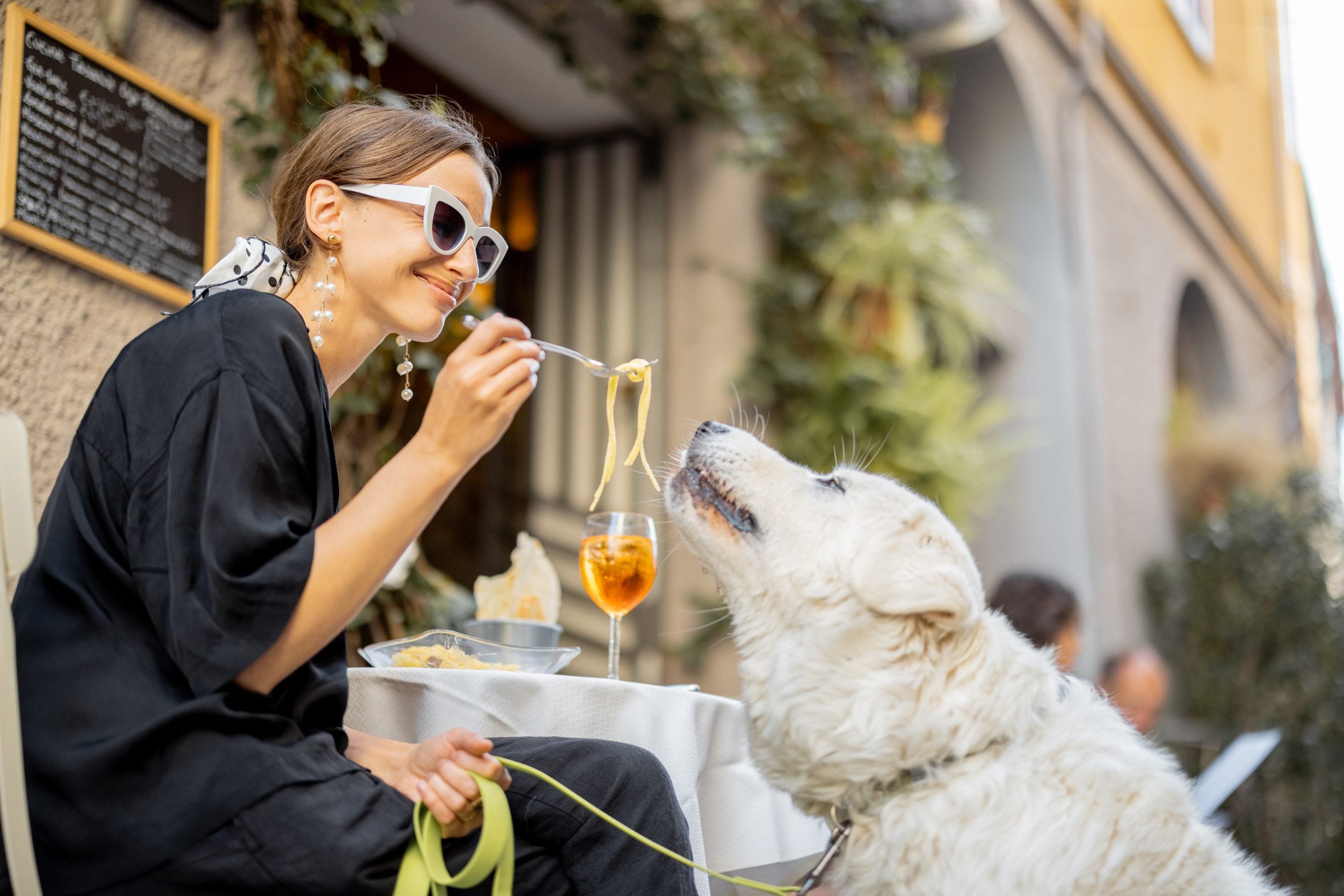 A woman enjoying pasta with her emotional support animal (ESA) at an outdoor cafe in New York, NY.