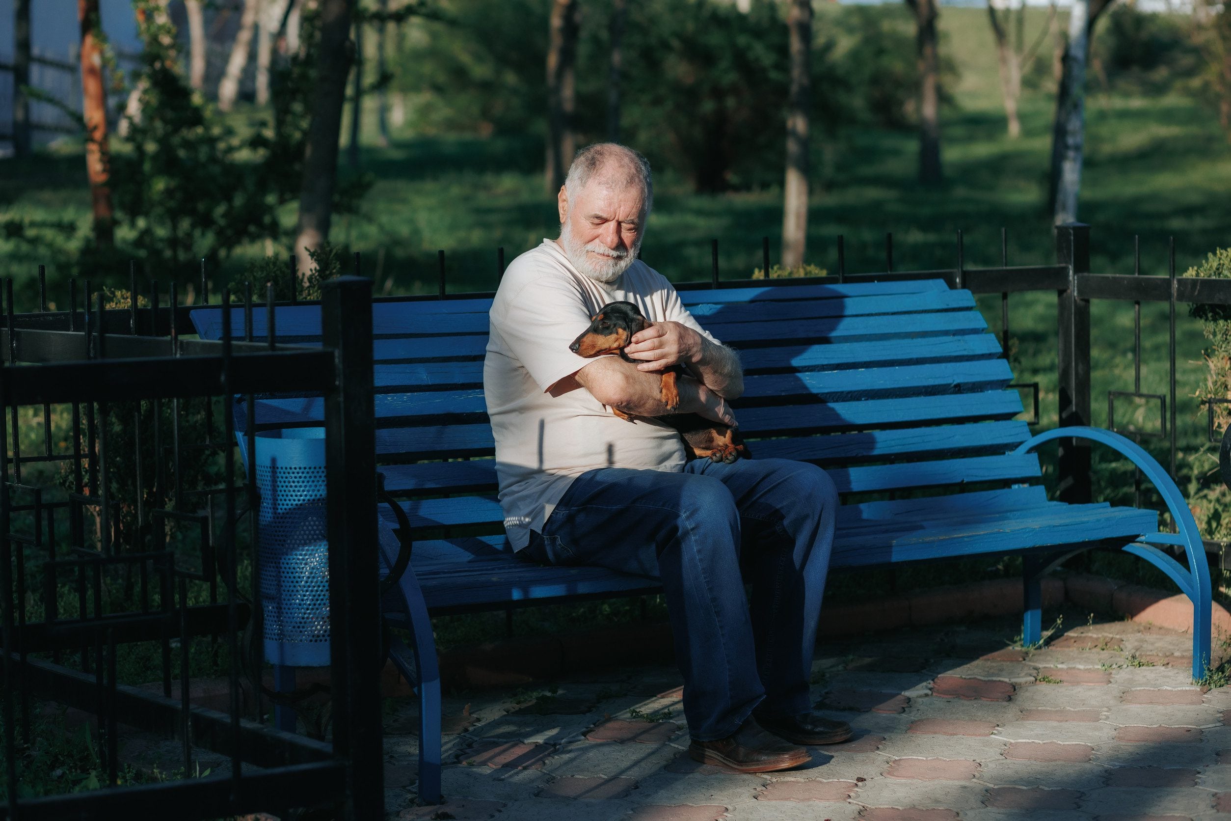 A man sitting on a blue bench while holding his emotional support animal dog in a park in Edmond, OK.