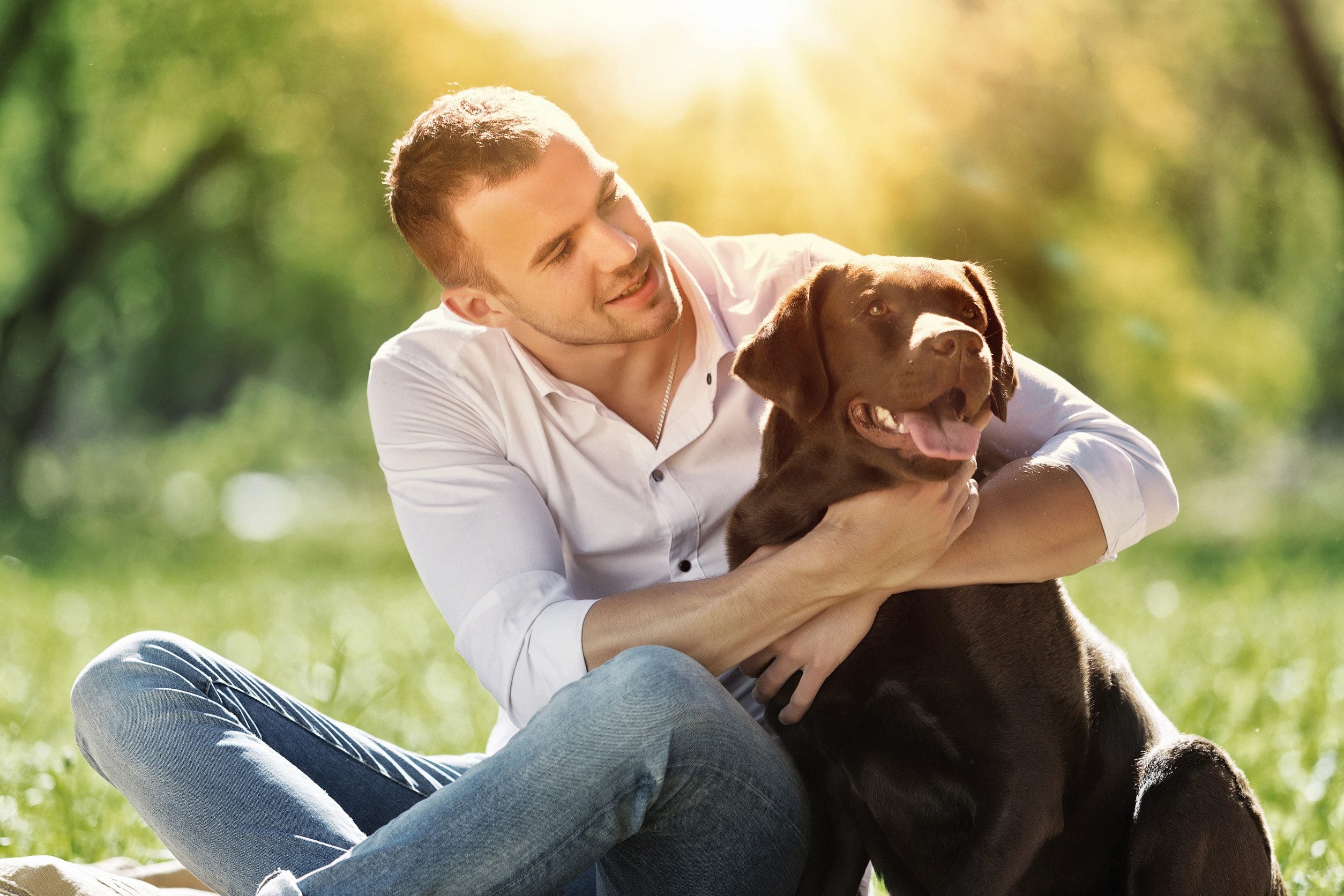 A happy man embracing his emotional support animal while relaxing in a park in Newark, NJ.