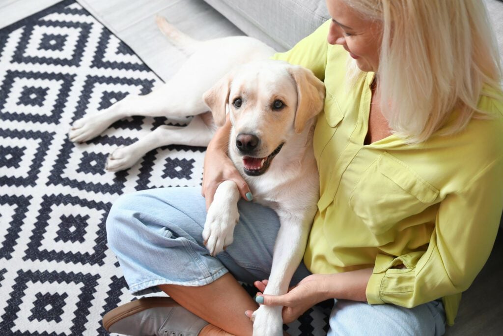 A woman sitting with a Labrador service dog on the floor, considering how to get a service dog for seizures.